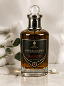 A bottle of Penhaligon's Halfeti Eau de Parfum with amber liquid, a black label with gold and red lettering, and a silver cap, set on a marble surface with soft white flowers in the background.